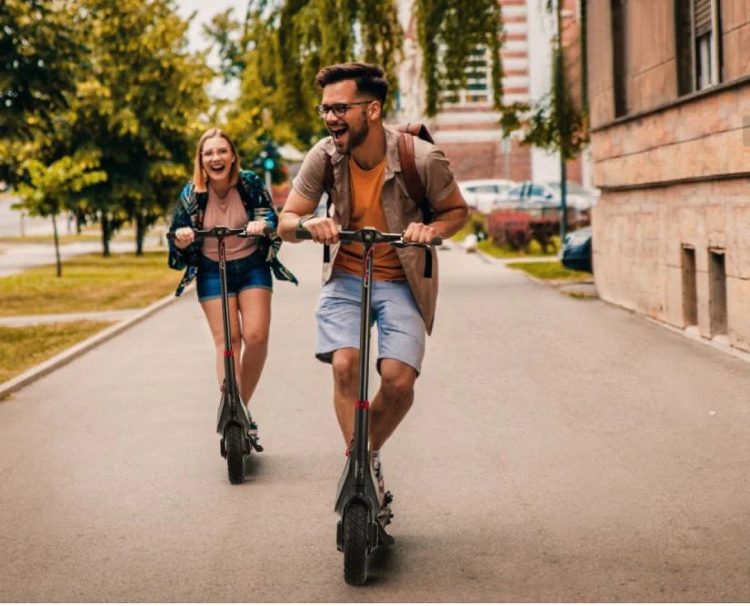 Two people riding electric scooters on a city street.