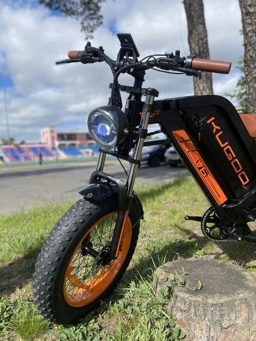 Electric bike with orange wheels parked on grass near a road