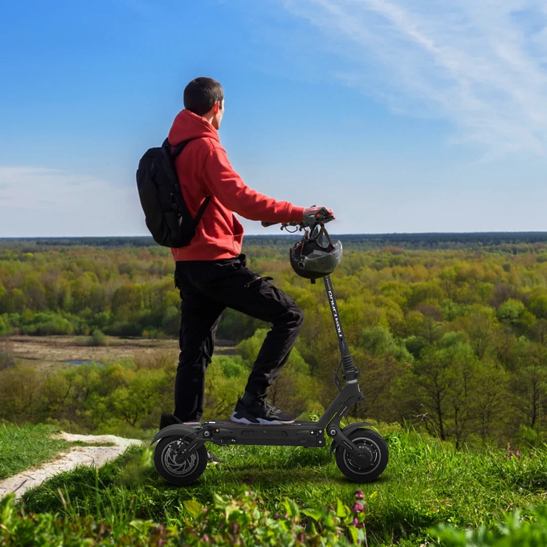 Person on a electric scooter with a helmet, standing on grass with a scenic background