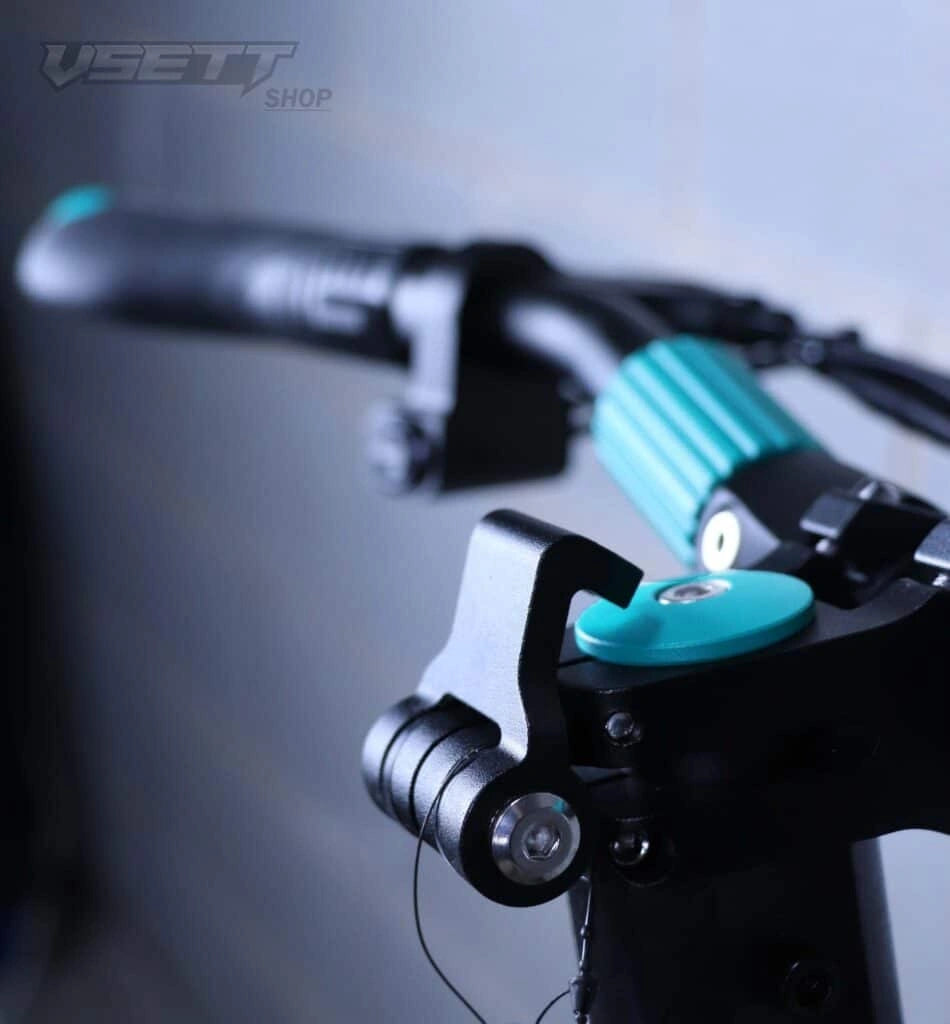 Close-up of a motorcycle handlebar with turquoise grips and controls against a blurred background.