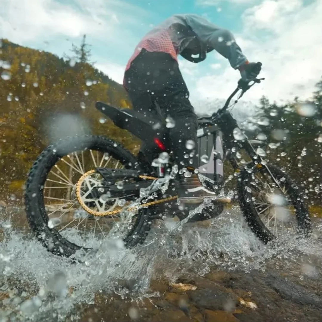 Person riding a motorcycle through water with trees in the background