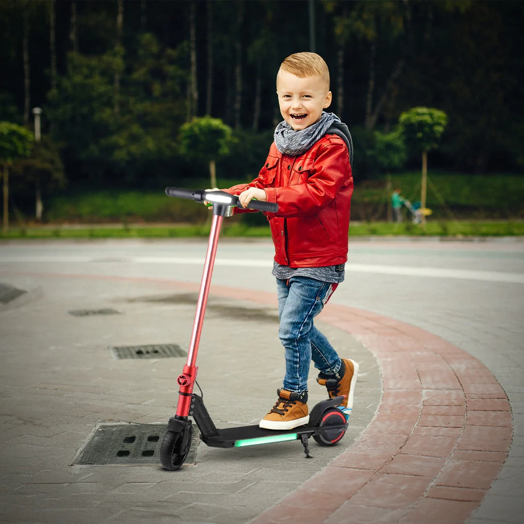 Child in a red jacket riding a scooter on a paved path with greenery in the background
