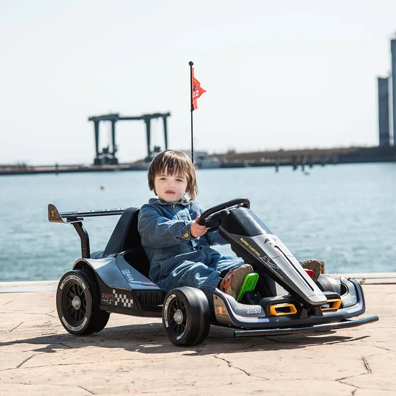 Child sitting in a go-kart by a waterfront with a bridge in the background