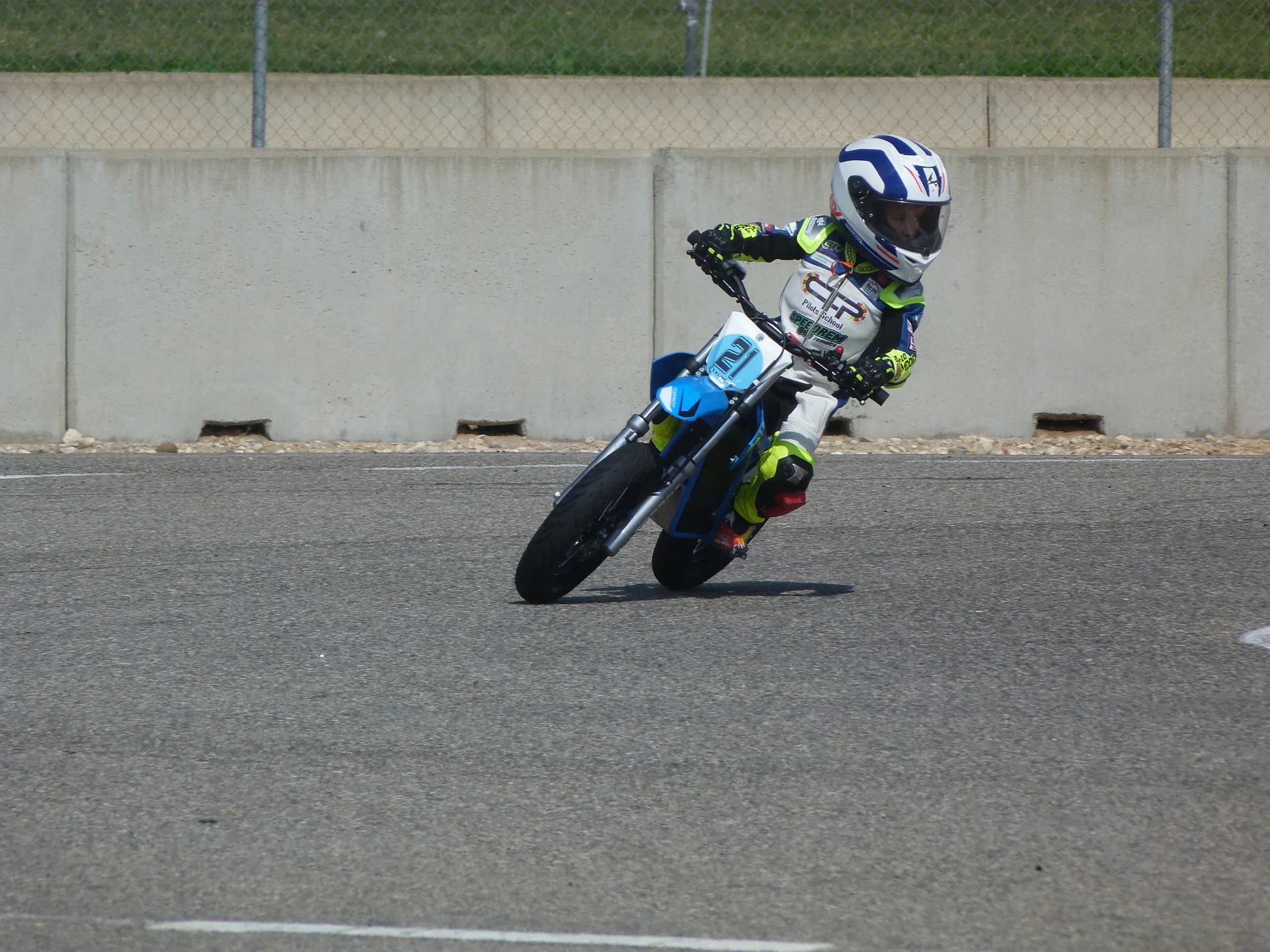 Person riding a motorcycle on a track with a concrete wall and grass in the background