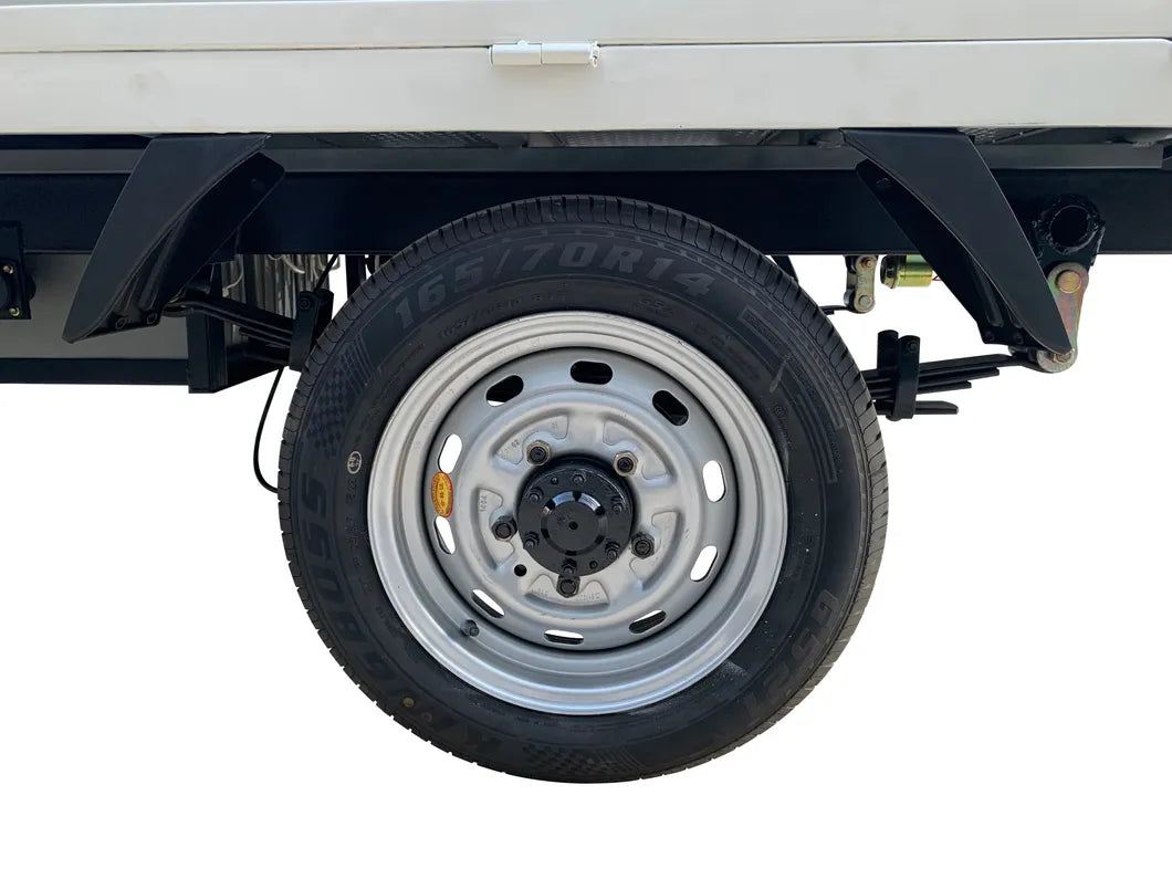 ocean cartz close-up detail of the rear wheel and tire on a white electric flatbed truck. The image highlights a silver steel rim with a black hub cap and a tire labeled "165/70R14", positioned beneath the white cargo bed. This detail shot emphasizes the robust utility tire and wheel assembly of the electric commercial vehicle or work truck.