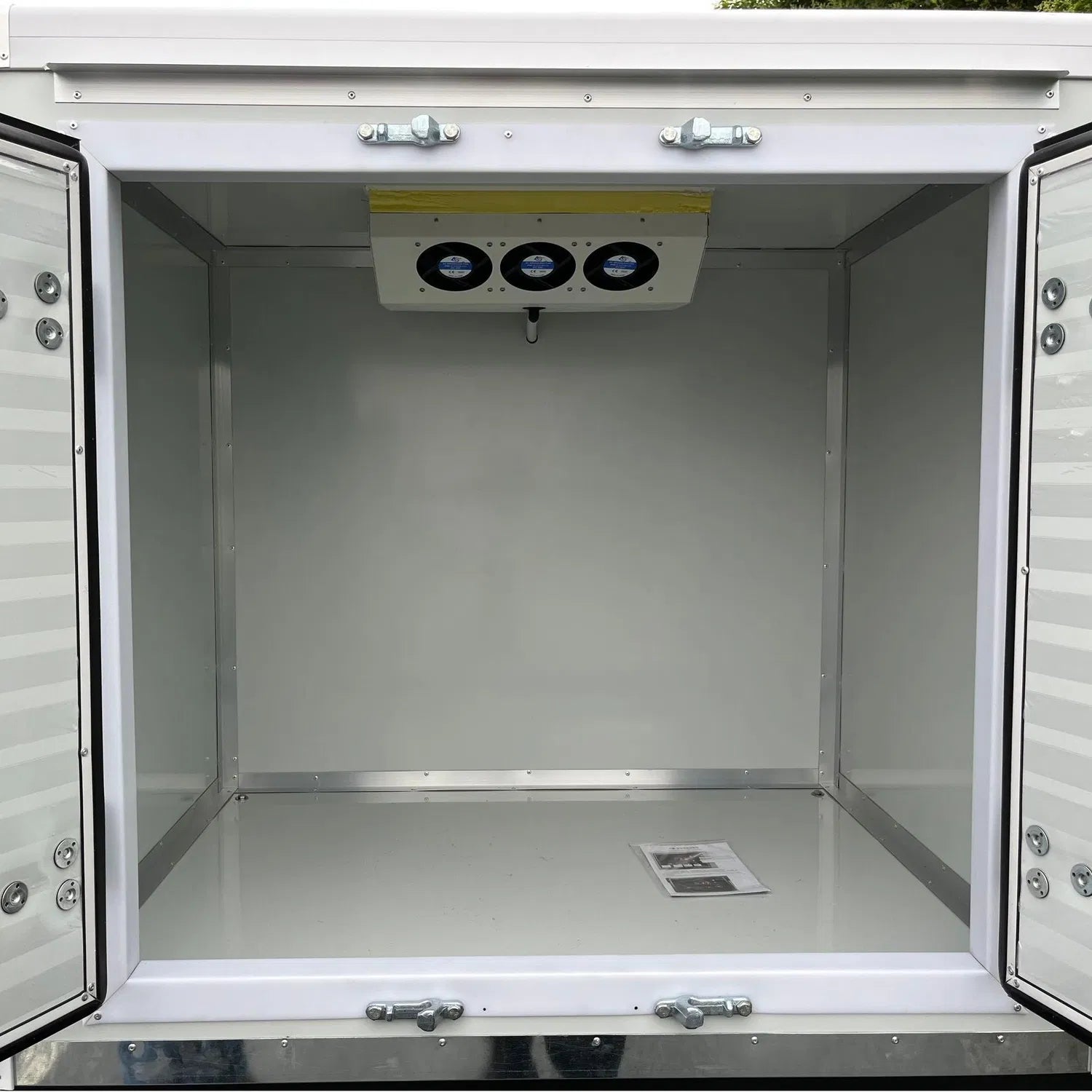 ocean cartz close-up rear view of the empty insulated cargo box interior of a white electric refrigerated delivery vehicle. The rear doors are open, revealing the smooth white walls, the three-fan cooling unit mounted near the ceiling, and the latching mechanisms. This image highlights the clean, temperature-controlled storage space for cold chain last-mile delivery.