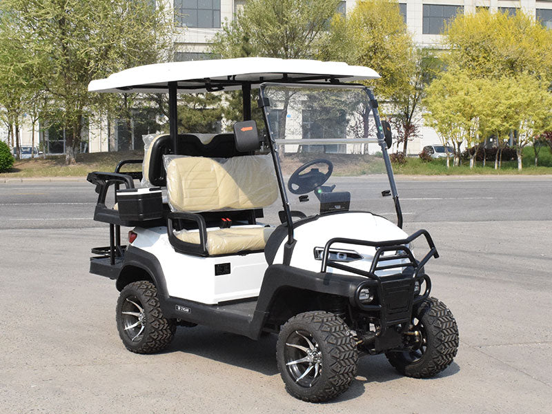 ocean cartz three-quarter front view of a white four-seater golf cart with a white roof, parked on an asphalt street. This lifted off-road electric vehicle features a black front brush guard, tan or cream-colored seats covered in plastic, and a rear cargo area with cup holders. The all-terrain golf cart is equipped with large, knobby off-road tires on custom black and silver wheels.