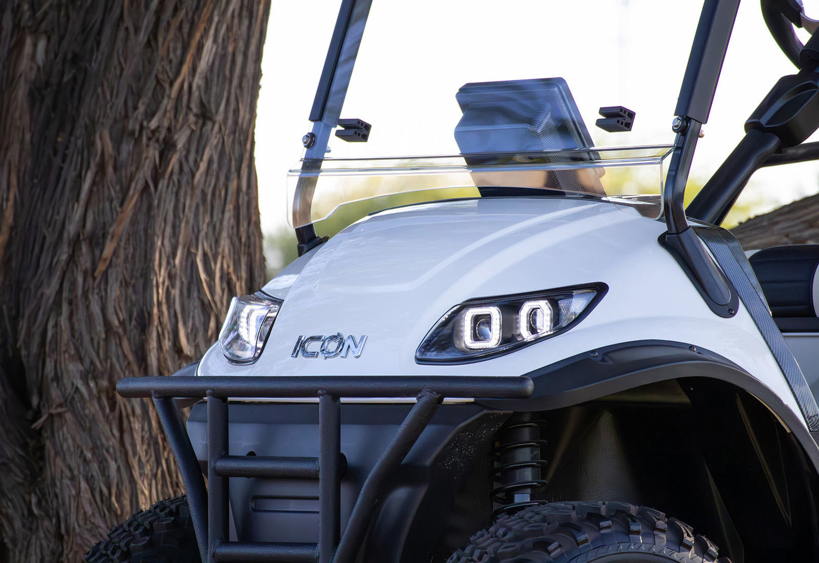 Close-up of a white UTV with 'Icon' branding, parked next to a tree.