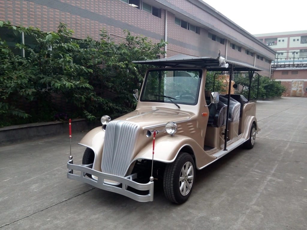 Vintage-style electric vehicle parked on a concrete surface with a building and greenery in the background.