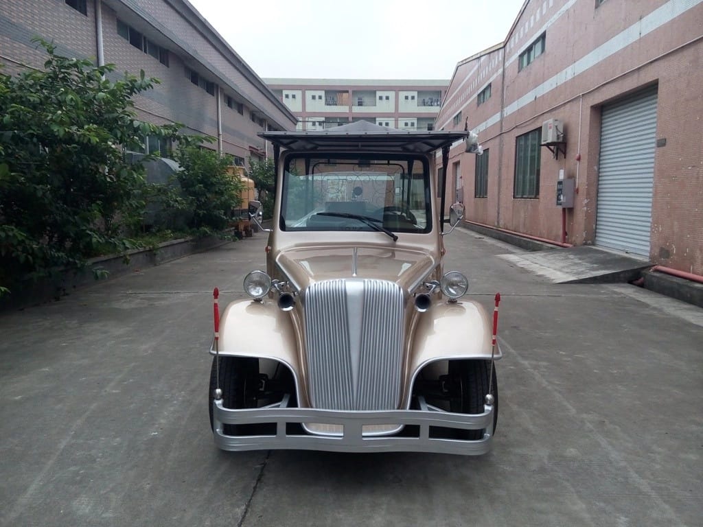 Vintage-style vehicle parked in an industrial area with buildings and trees in the background.