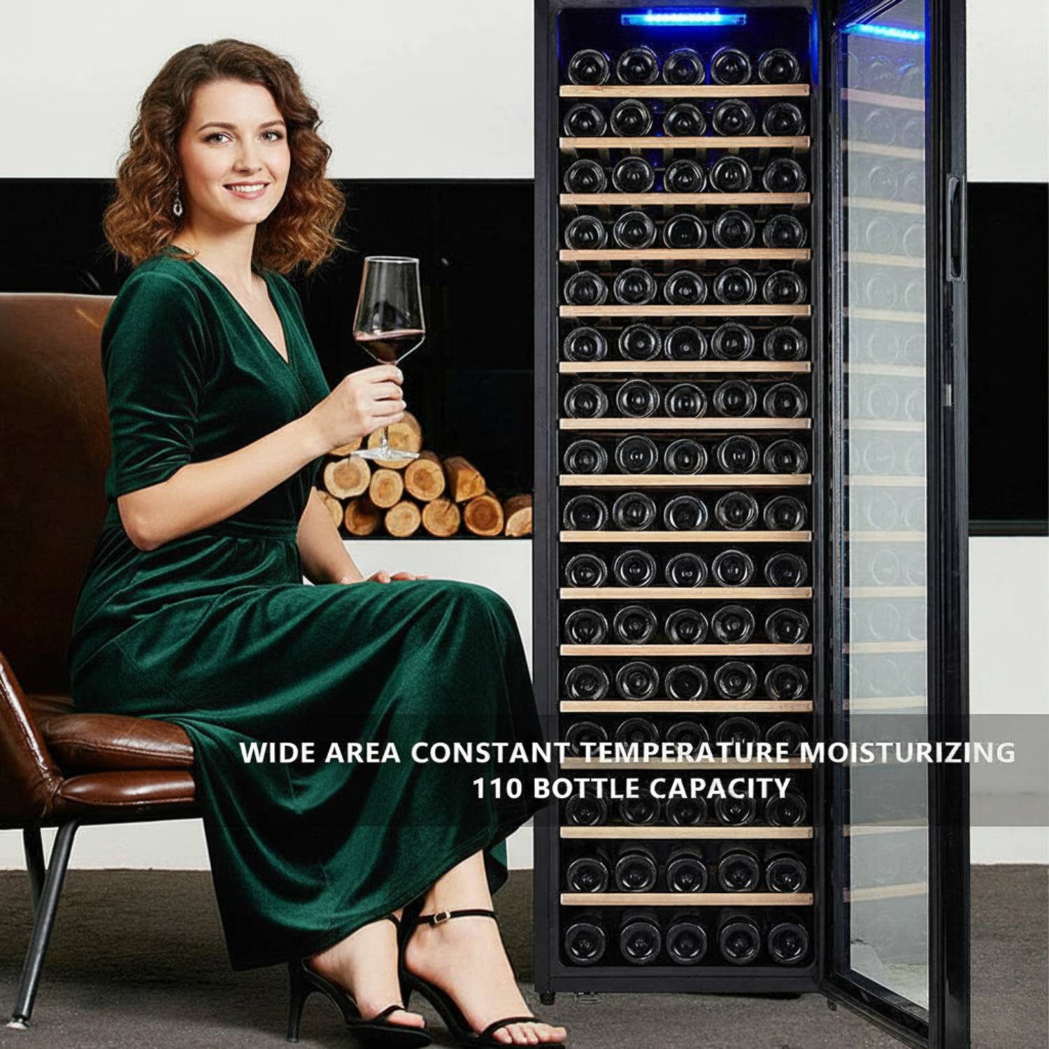 Woman in a green dress holding a glass of wine next to a large wine cooler.