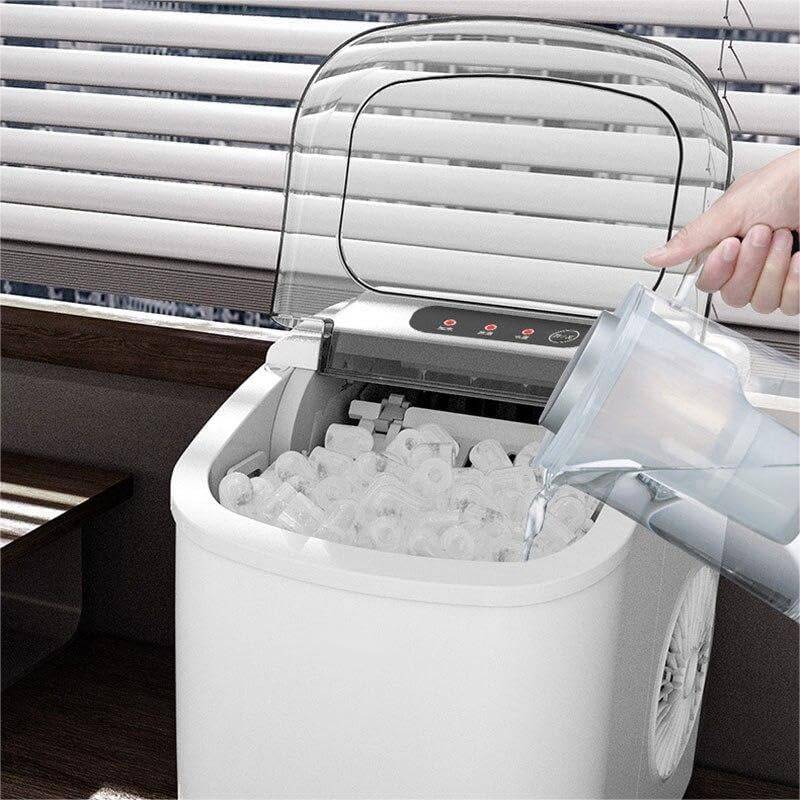 Ice maker with a hand pouring water into it, set against a window with blinds.