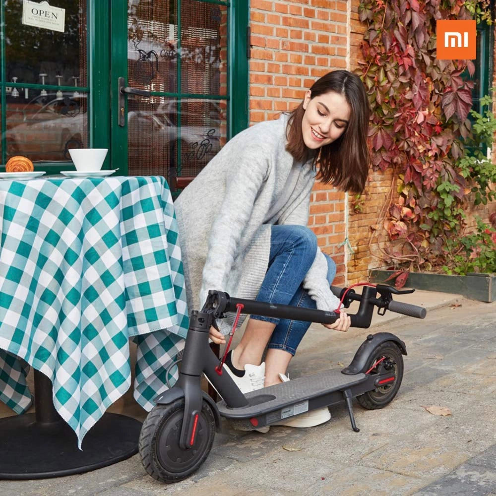 Woman sitting on a scooter next to a table with a checkered tablecloth in an outdoor setting.