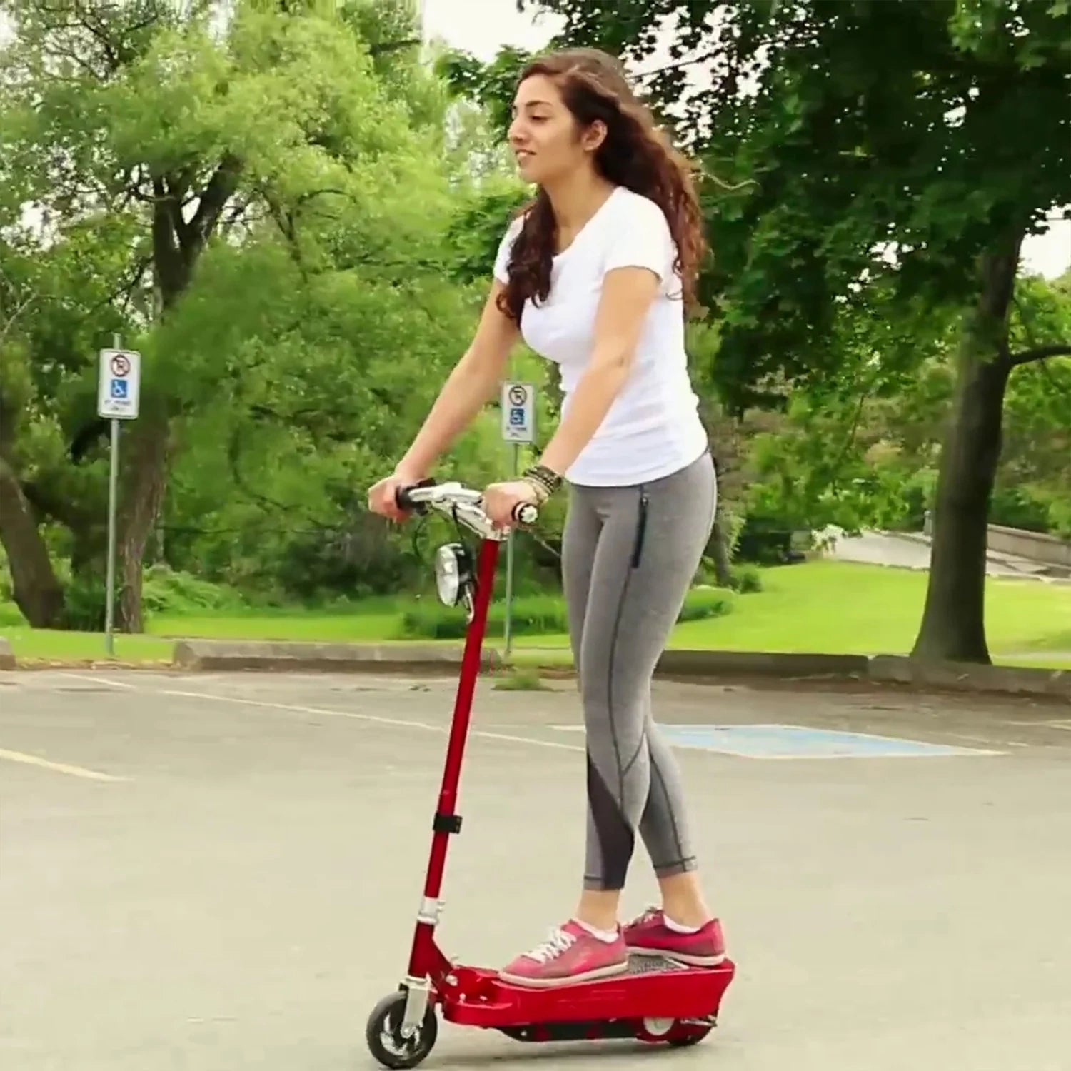 Woman riding a red scooter on a road with greenery in the background