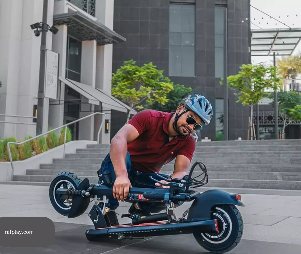 Person riding a scooter in an urban setting with modern buildings and stairs in the background.