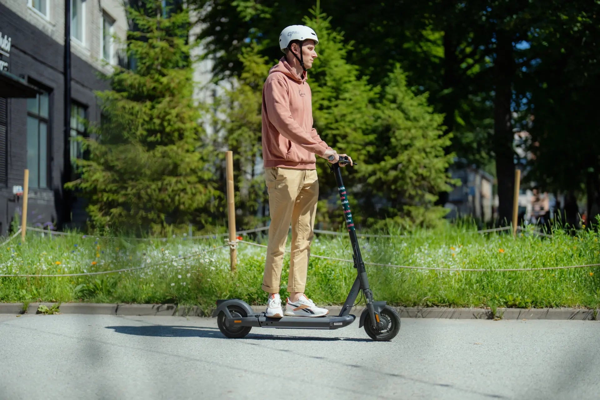 Person riding an electric scooter on a city street with greenery in the background