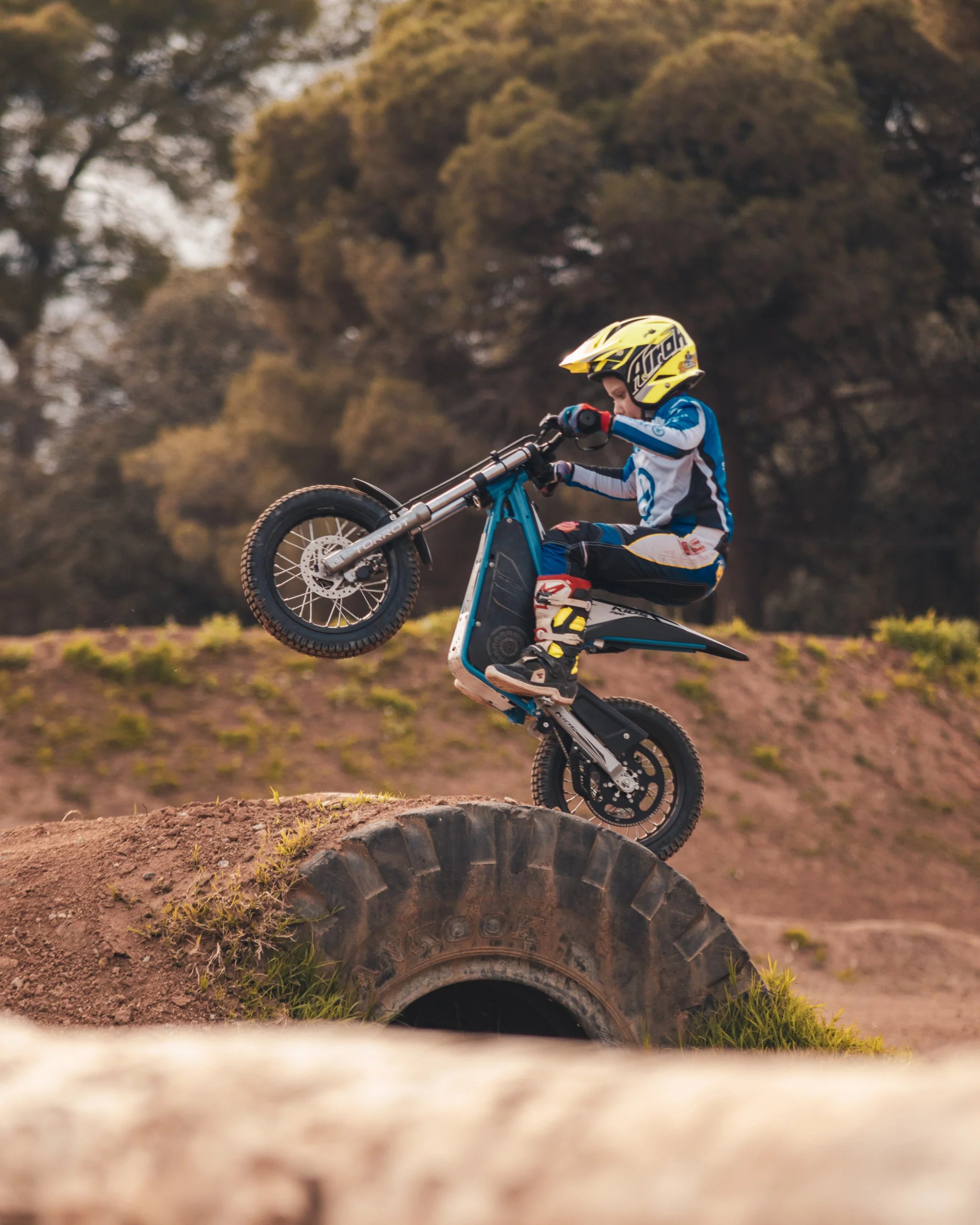 Person on a dirt bike performing a jump over a dirt mound with trees in the background