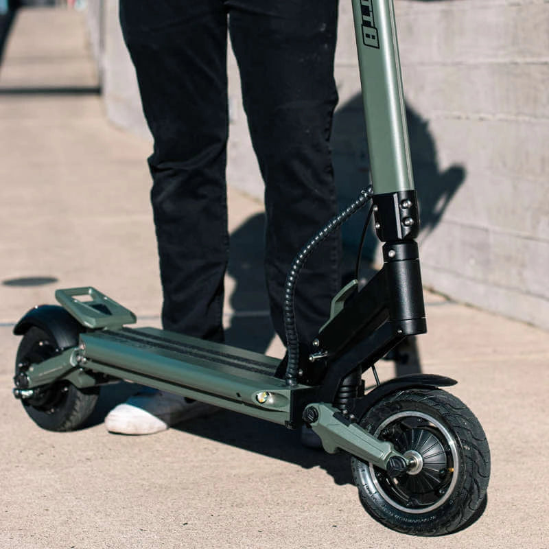 Person standing next to a green electric scooter on a sidewalk.