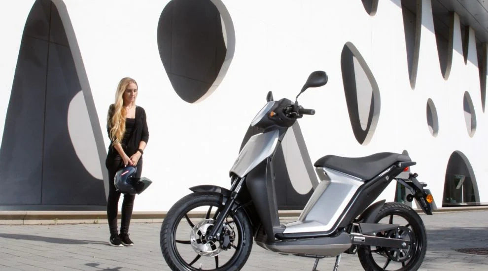 Woman standing next to a modern electric scooter with a futuristic building in the background