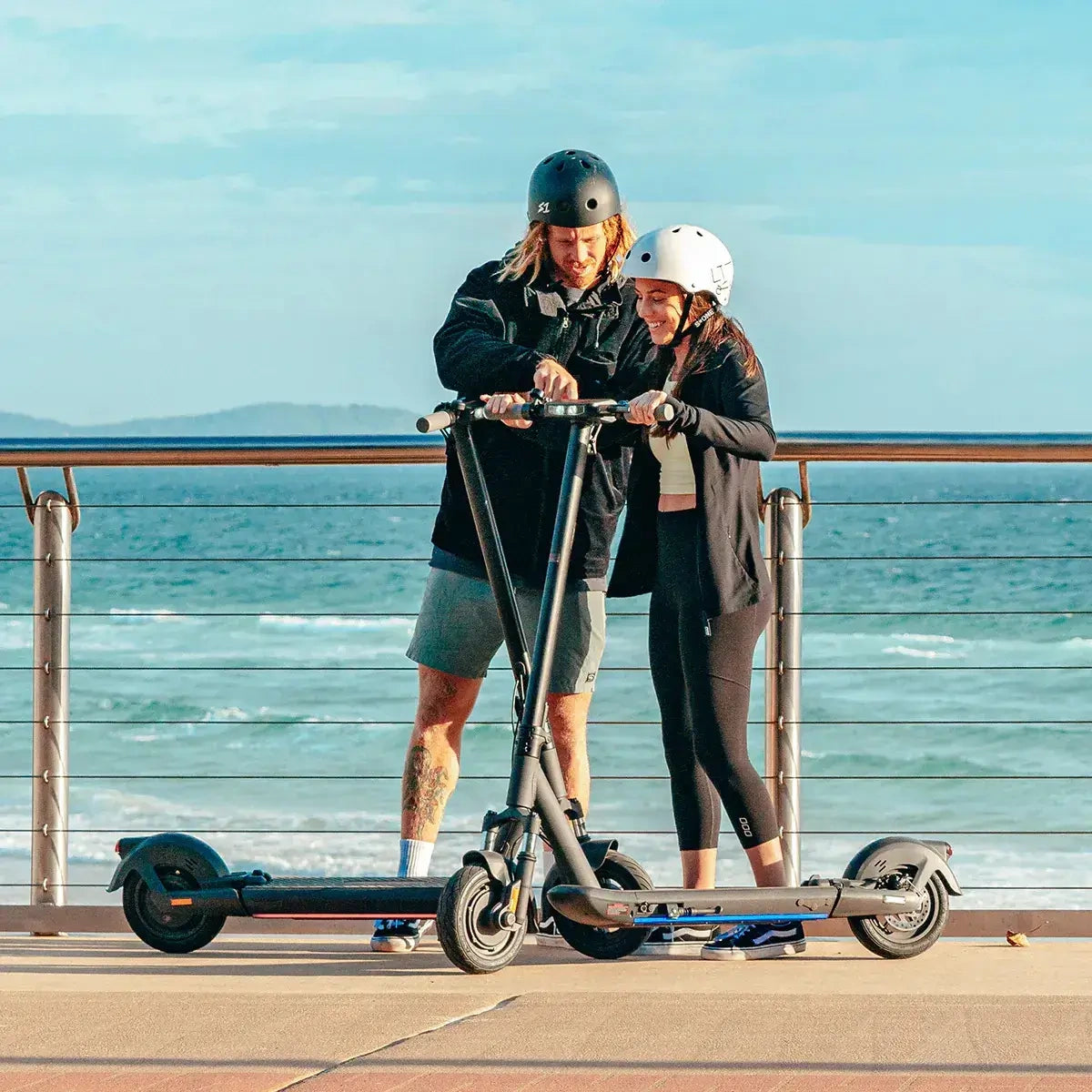 Two people with electric scooters by the sea