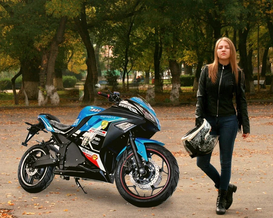 Woman walking with a helmet next to a blue and black motorcycle in a park.