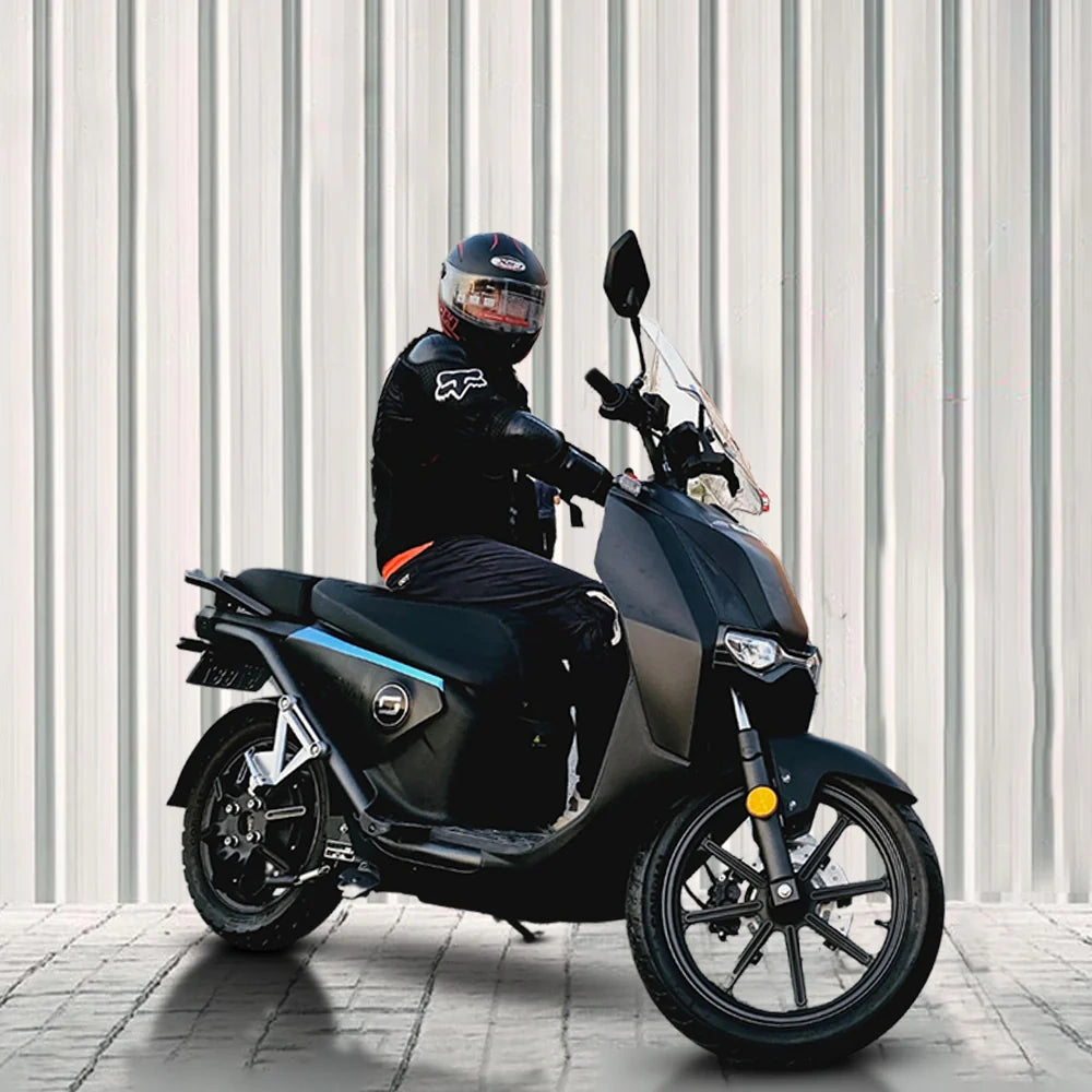 Person sitting on a black scooter against a light-colored wall.