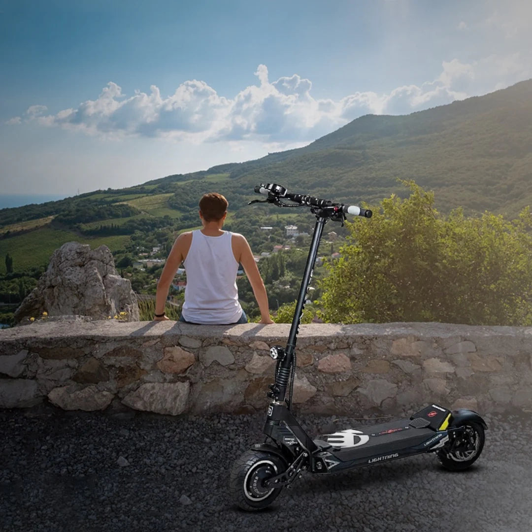 Person sitting on a stone wall with an electric scooter in front of them, overlooking a scenic landscape.