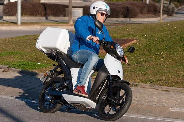 Person riding a white scooter on a road with grass and a sidewalk in the background
