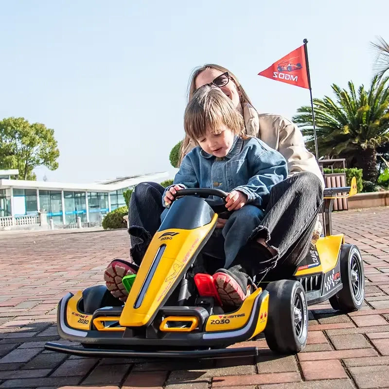 Child and adult in a yellow and black toy go-kart on a sunny day.