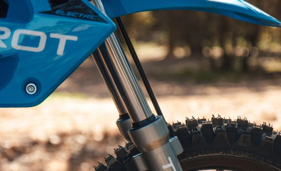 Close-up of a blue electric motorcycle with 'HOT' branding on a blurred natural background.