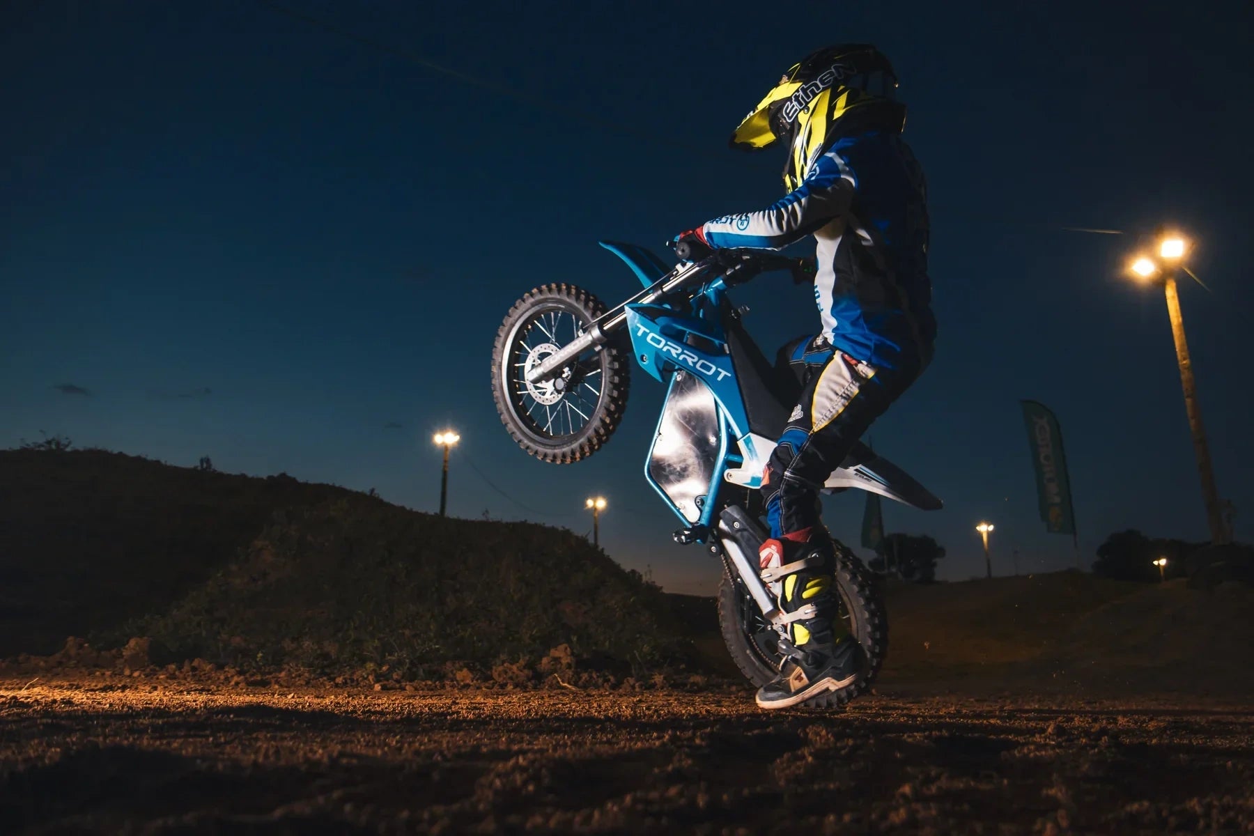 Motorcycle rider performing a stunt on a track at night with lights in the background