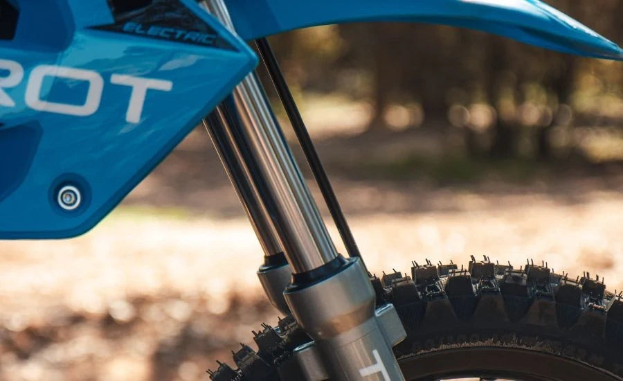 Close-up of a blue electric dirt bike with 'HOT' branding on a blurred natural background.