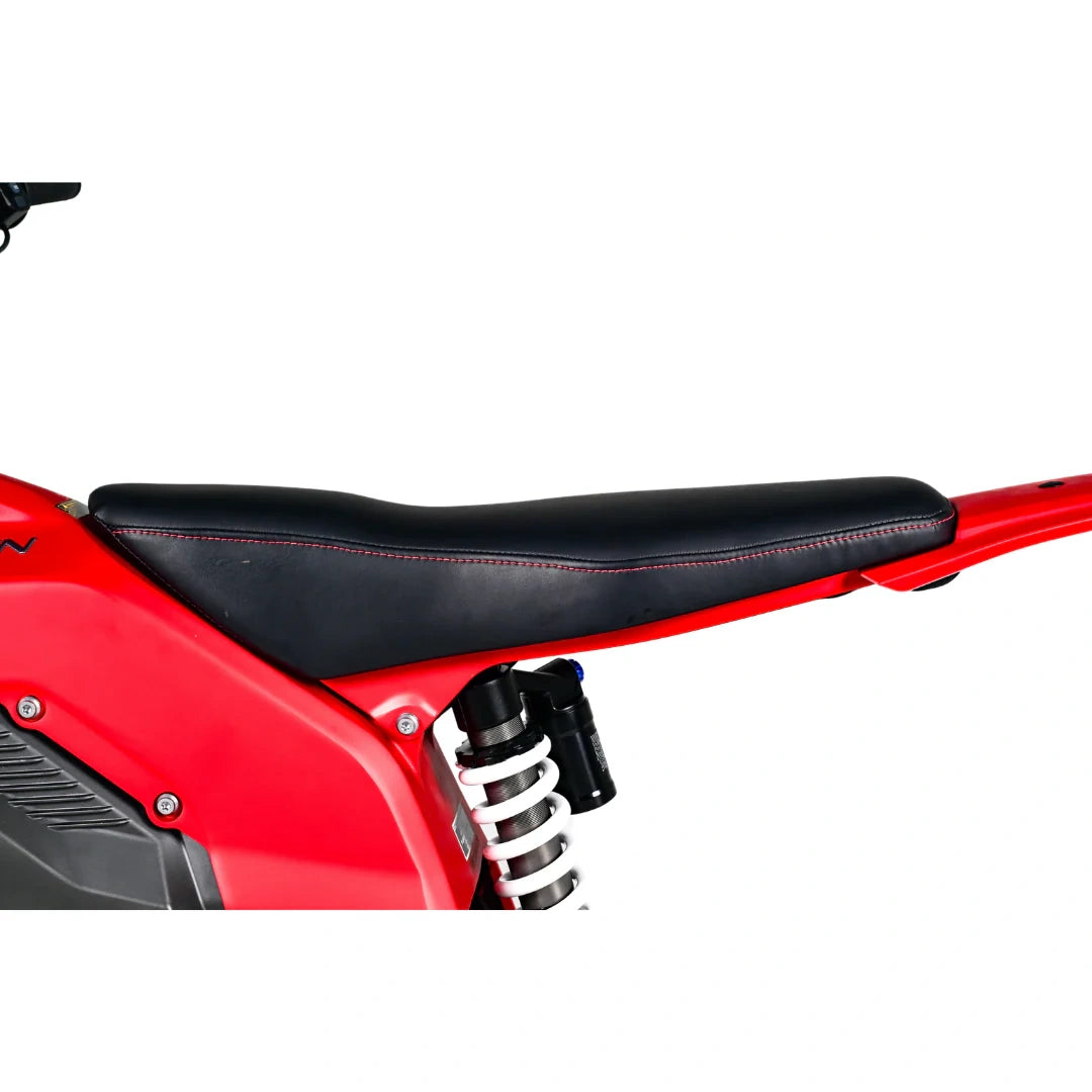 Close-up of a red motorcycle with a black seat and suspension on a white background