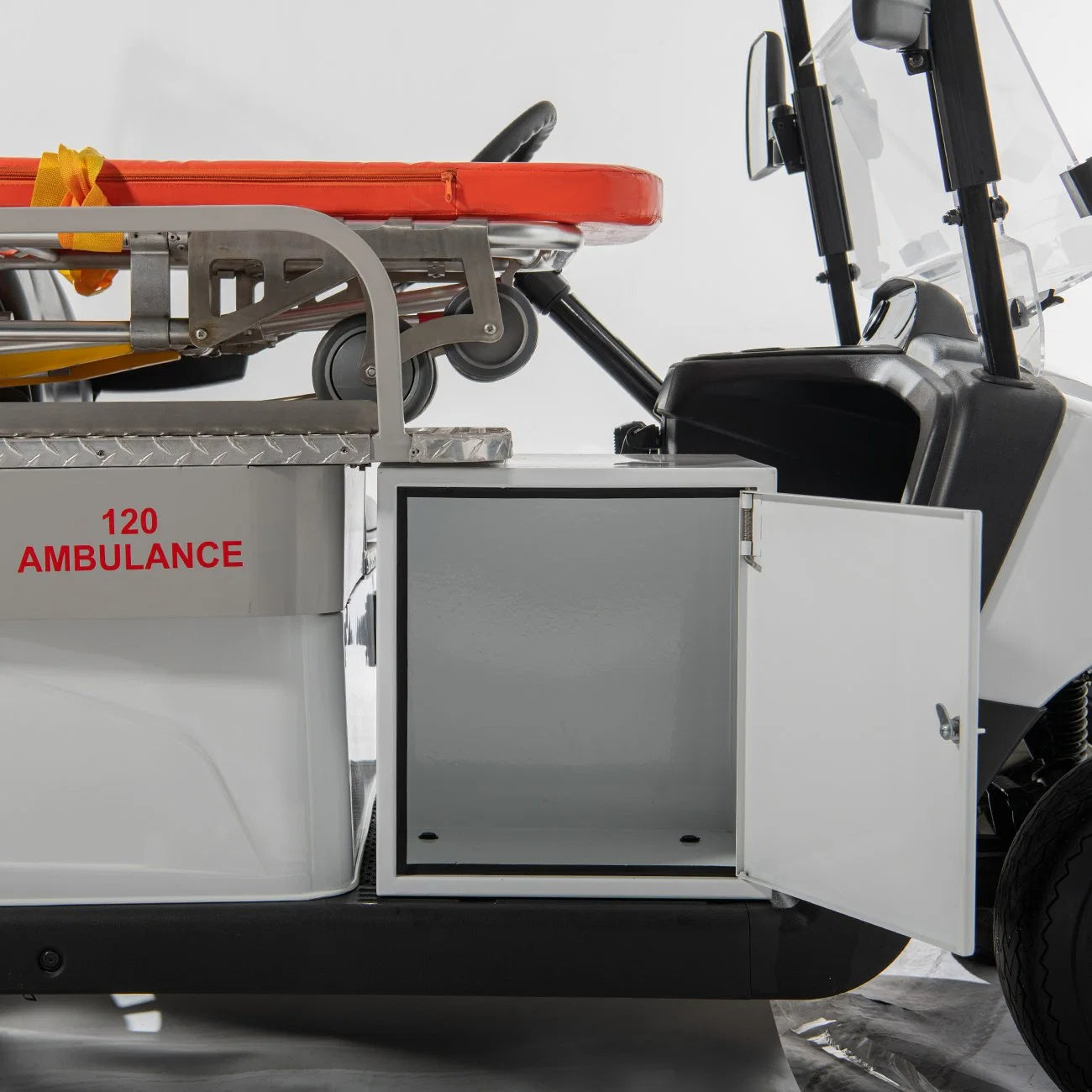 ocean cartz close-up detail of the storage cabinet on the side of a white ambulance golf cart. The small, white cabinet door is open, revealing the empty interior space for medical supplies. The side panel is labeled "120 AMBULANCE" in red text, with the stretcher visible above, highlighting the specialized medical utility vehicle's practical design for emergency response.