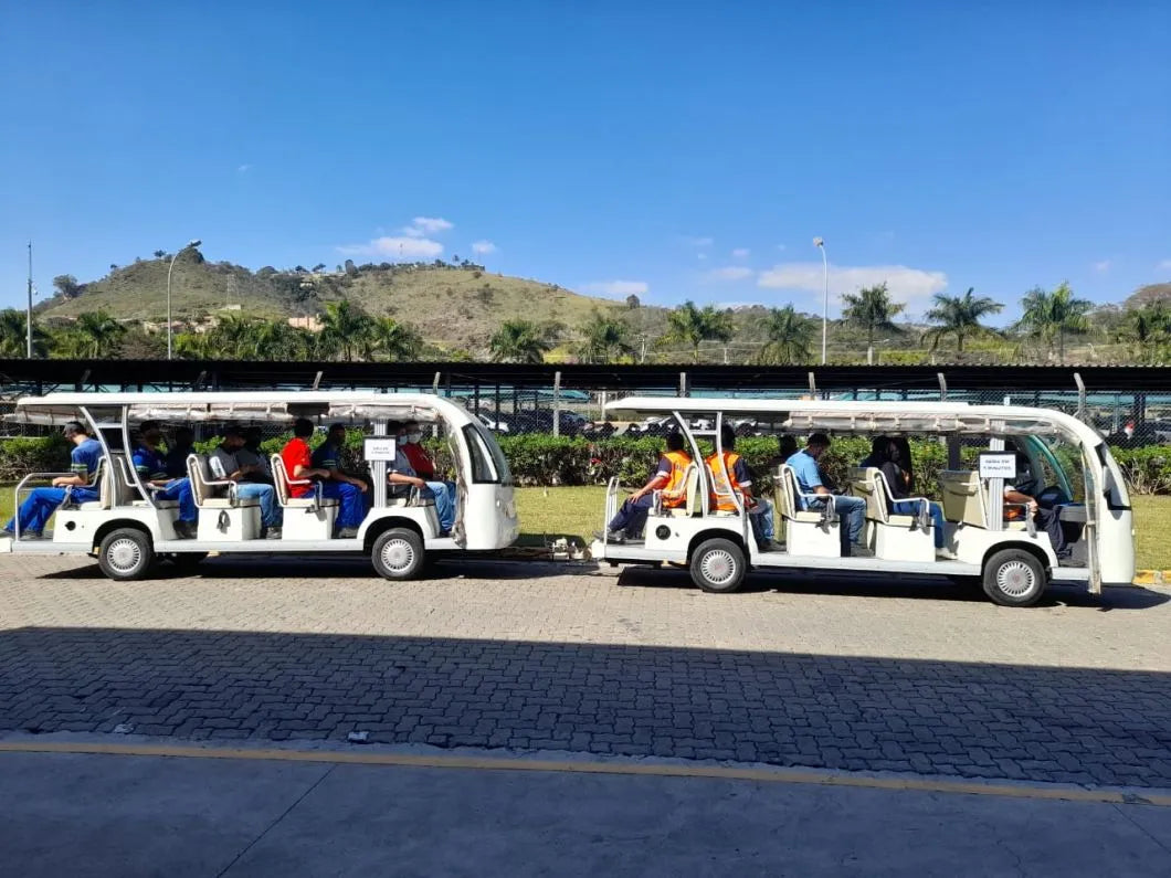 Two white electric buses with passengers on a road with a scenic background.