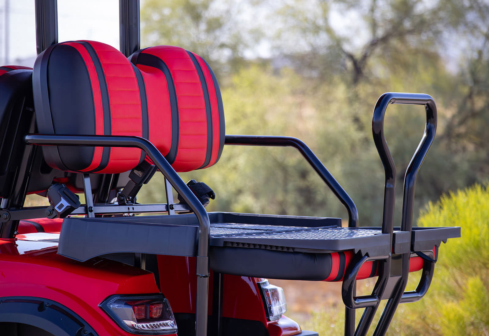 Red and black golf cart with a tray attached to the back, set against a blurred natural background.