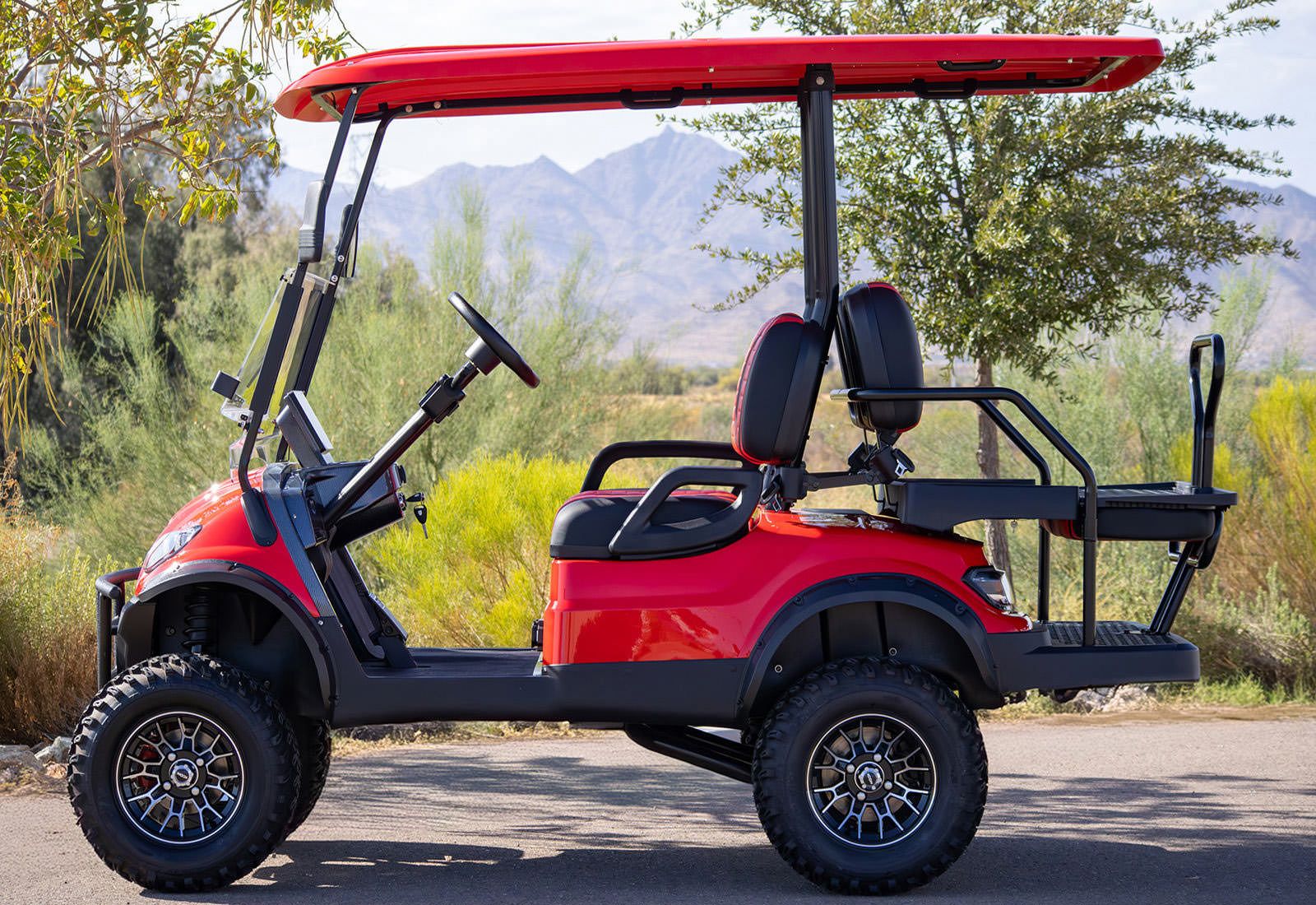 Red golf cart on a road with mountains and trees in the background