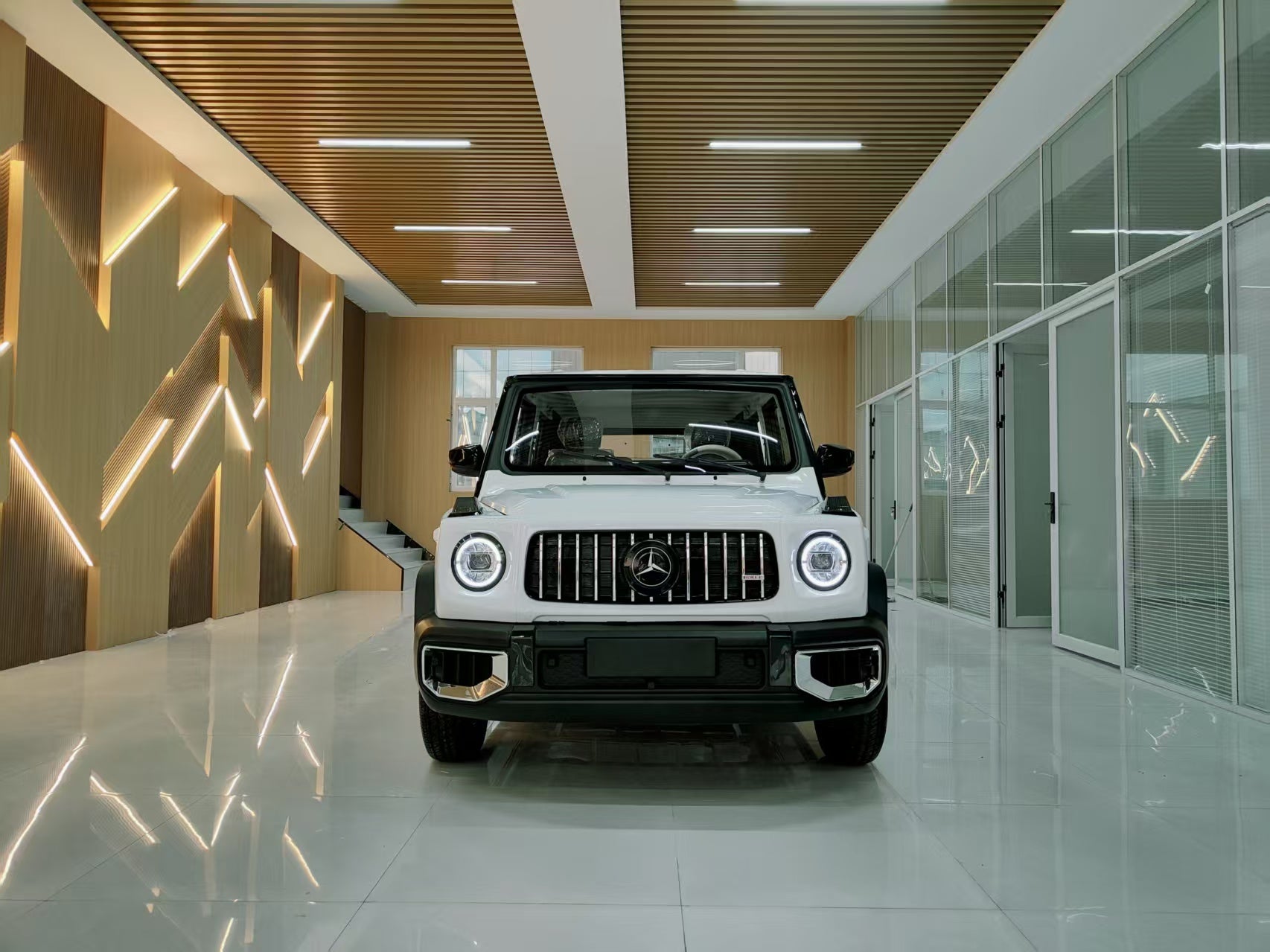 White Mercedes-Benz G-Class SUV in a modern showroom with wooden ceiling and glass walls.