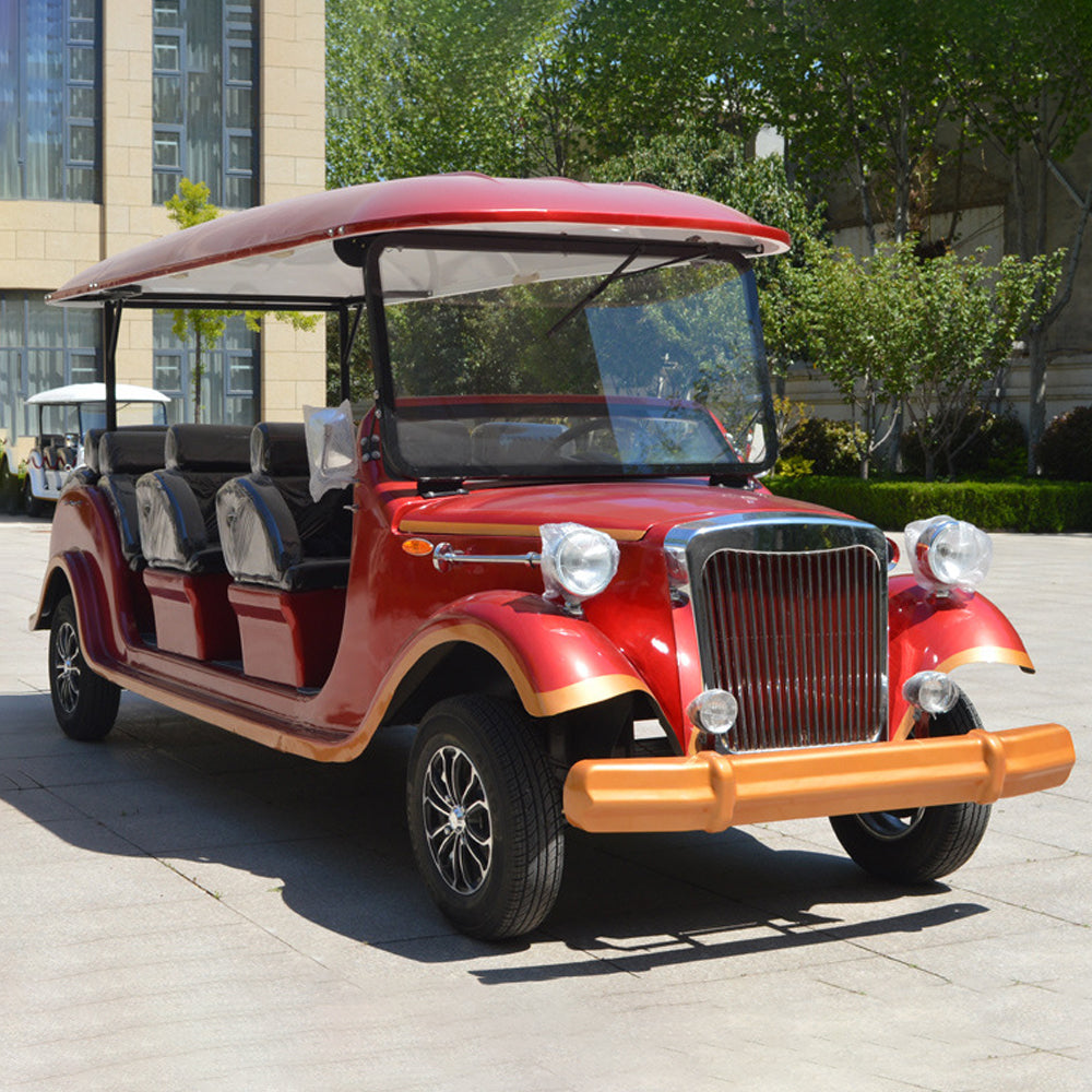 Red vintage-style electric vehicle on a paved area with trees and buildings in the background