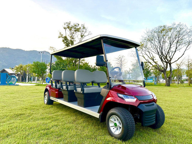 Red electric golf cart with multiple seats on a grassy area with trees and mountains in the background.