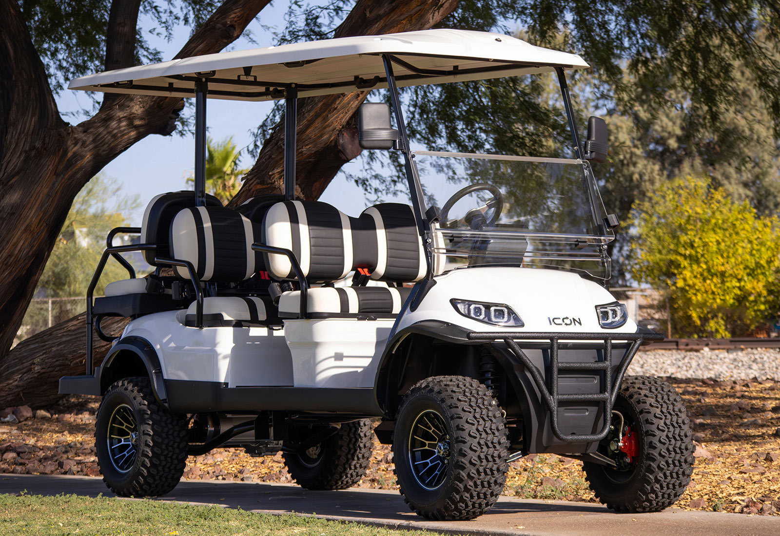 White golf cart with black seats parked on a path with trees in the background