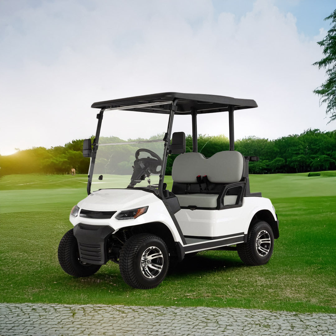 ocean cartz three-quarter front view of a white four-seater golf cart with a black roof, parked on a lush green golf course. This electric vehicle features gray seats, a full windshield, and a modern front design with black accents. The lifted golf cart is equipped with all-terrain tires and custom black and chrome wheels, shown in a wide-open outdoor setting with trees and a sunny sky, highlighting its use as a luxury golf cart.