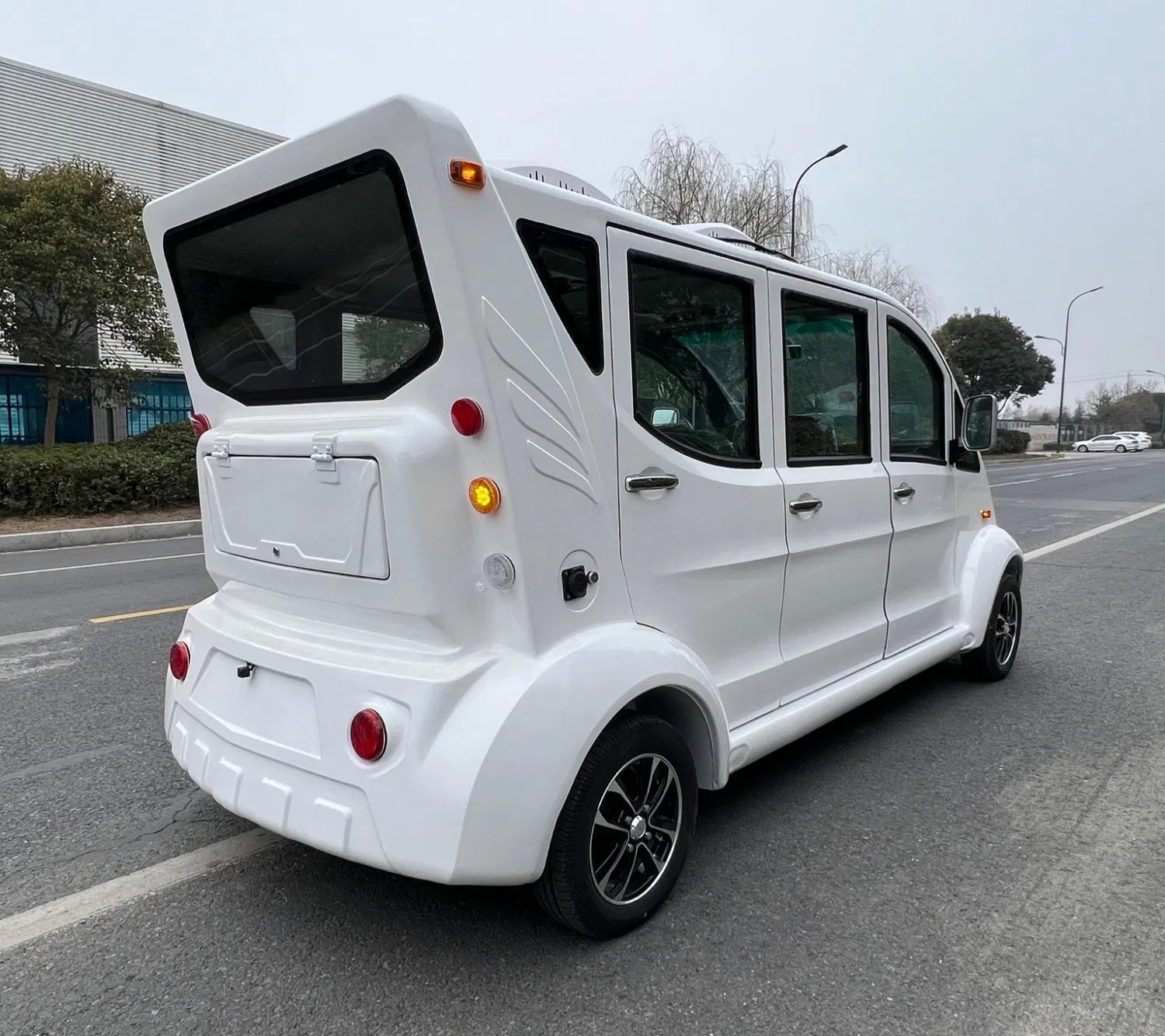 White electric vehicle on a road with a building and trees in the background