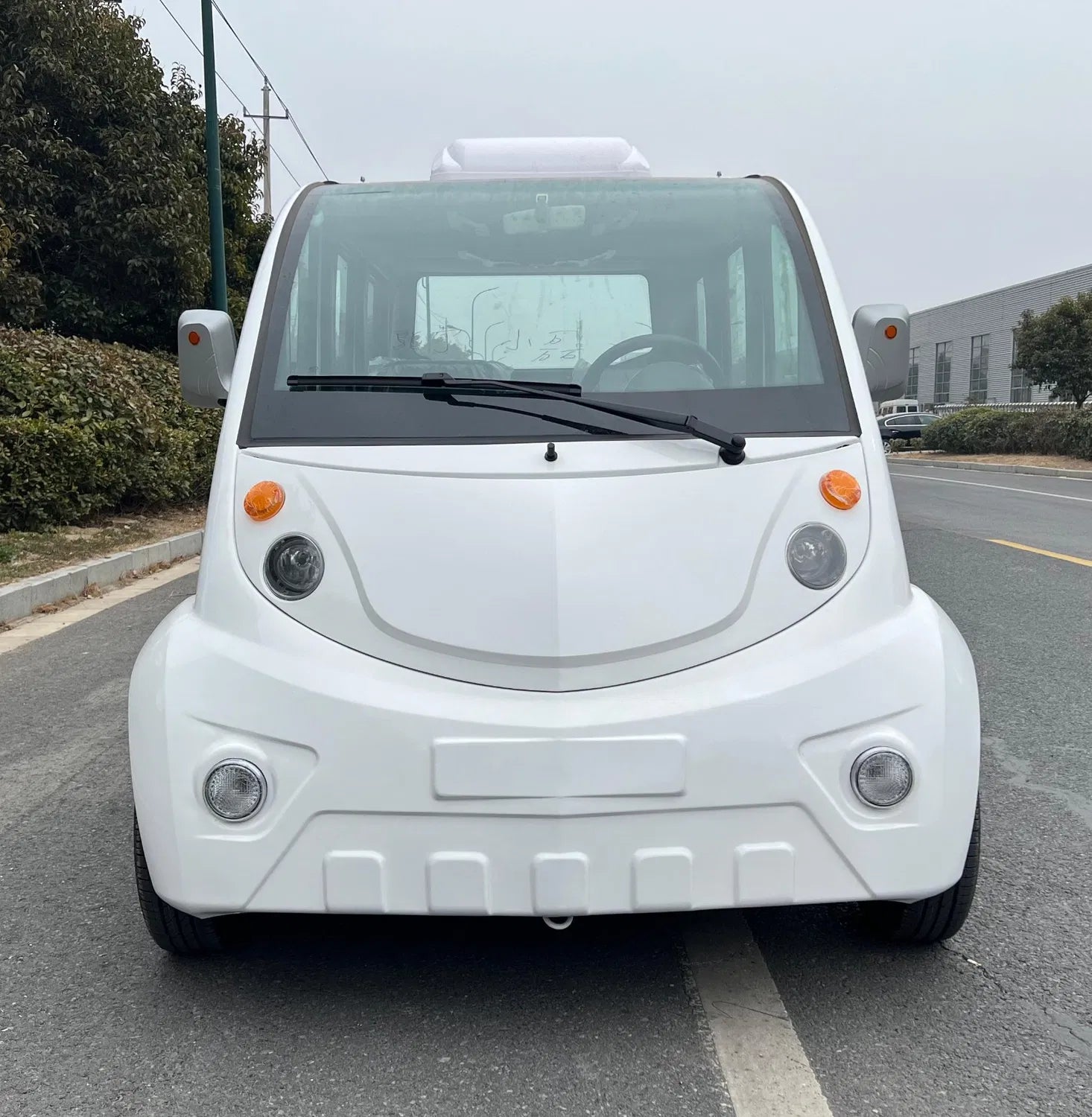 White electric vehicle on a road with trees and buildings in the background