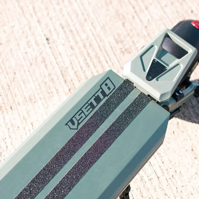 Close-up of a green and black electric skateboard with 'VEE' branding on a textured surface.
