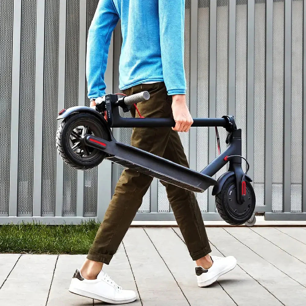 Person carrying a folded electric scooter outdoors.